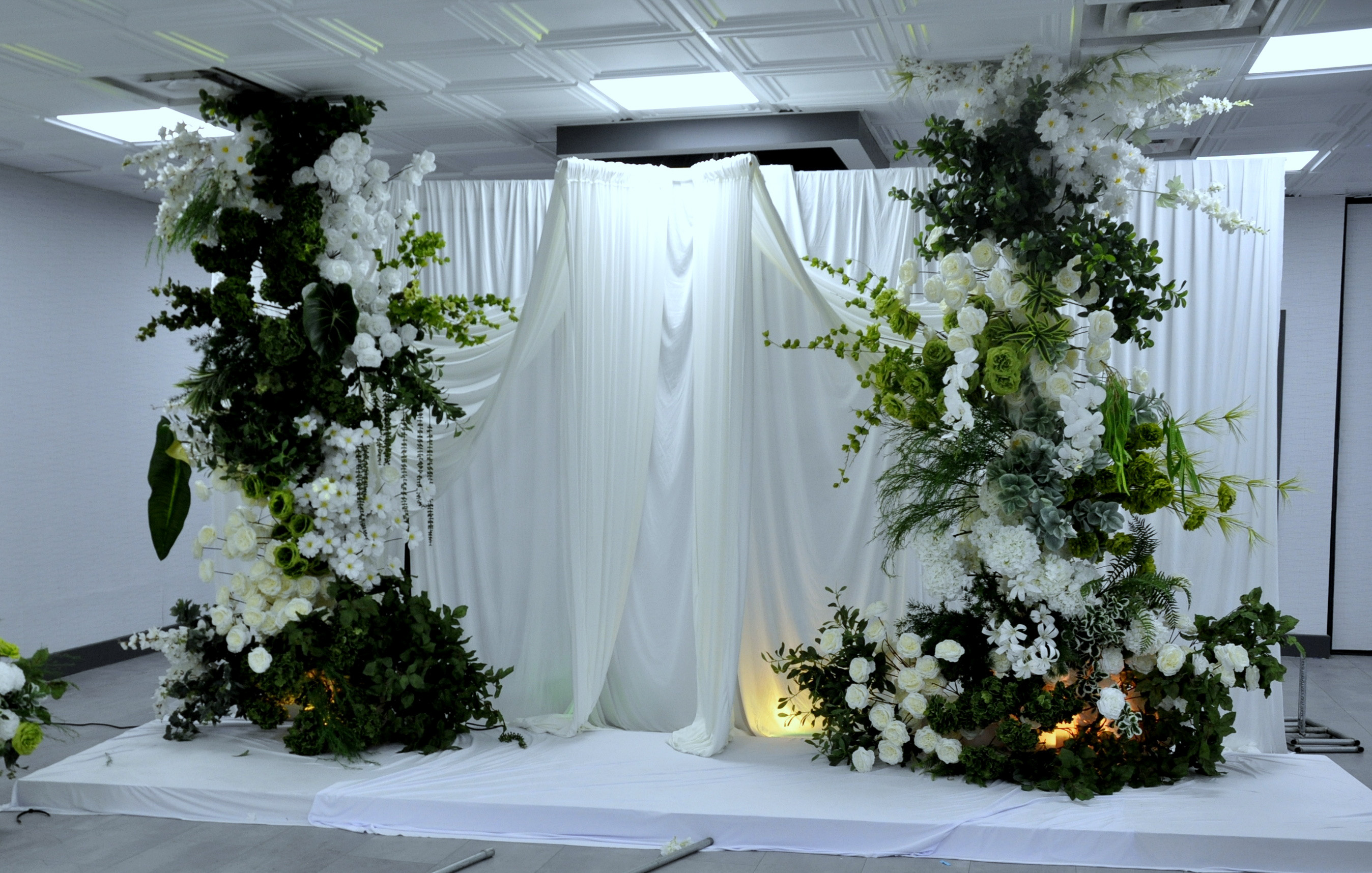 Brightly lit floral ceremony installation with white draping